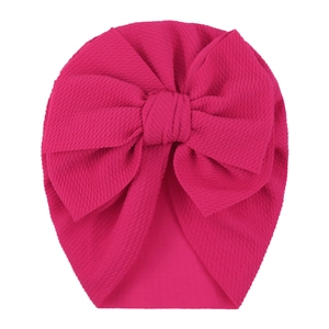 Detail of rose red infant turban hat featuring textured fabric and a large bow