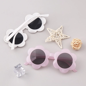 Flat lay detail of cute sunflower flower-shaped kids sunglasses in white and pink