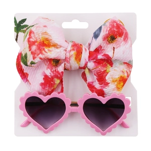 Close-up of baby girl summer set with floral bow headband and pink heart sunglasses