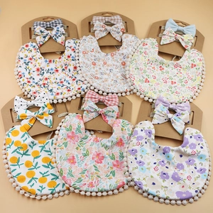 Detail view of 6-piece baby bib and floral headband set with pom-pom trim on warm background