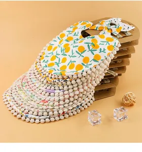 Détail de bavoir et bandeau pour bébé avec imprimé orange et bordure à pompons crème