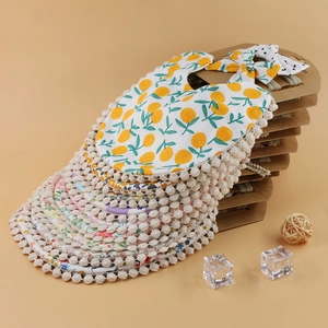 Detail view of cotton baby bibs with floral prints and white pom-pom trim in packaging