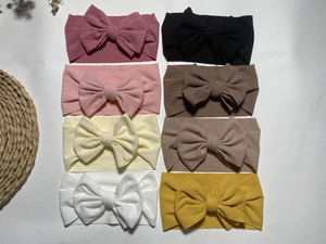 Flat lay of eight colorful elastic ribbed baby headbands with large bows on white background