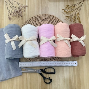 Close-up of five rolled bamboo cotton baby swaddle blankets with ribbon ties on wood