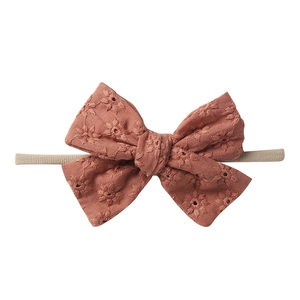 Detail of baby headband with hollow embroidery bow in brick red and nylon elastic band