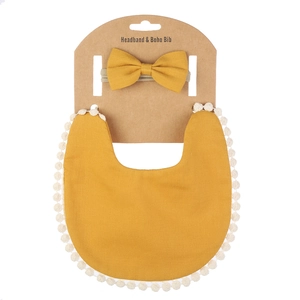 Détail d'un bavoir boho jaune moutarde avec bordure à pompons blancs et bandeau assorti