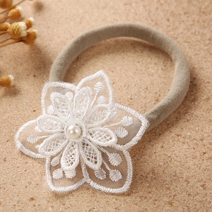 Close-up of baby nylon headband featuring an embroidered lace flower with a pearl center