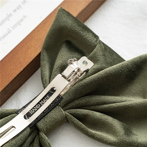 Macro shot of dark green velvet bow hair clip with metal spring clip and handmade label