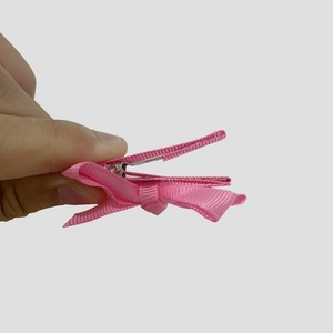Detail of pink floral bow hair clip being held to show the metal duckbill clamp mechanism