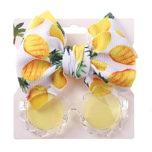 Detail von Baby-Blumen-Sonnenbrille und Ananas-Schleife-Stirnband auf Karton