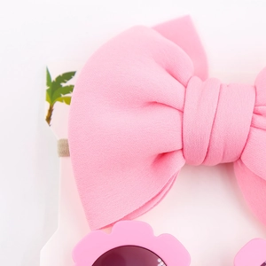 Dettaglio della fascia con fiocco in cotone rosa e occhiali da sole a fiore per neonati