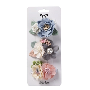 Détail de trois pinces à cheveux fleurs en tissu avec perles sur carte blanche