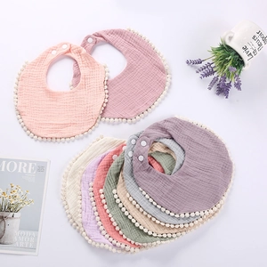 Detail of soft muslin cotton baby bibs with pom-pom trim and adjustable snap buttons