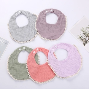 Close-up of muslin cotton baby bibs with pom-pom trim and adjustable snap buttons
