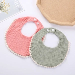 Detail of baby cotton muslin bibs with pom-pom trim and adjustable snap buttons