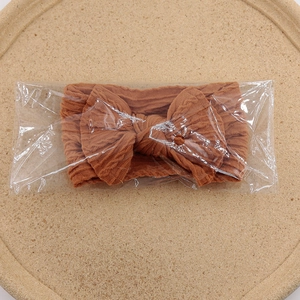 Vue détaillée du bandeau à nœud jacquard caramel dans son emballage plastique transparent