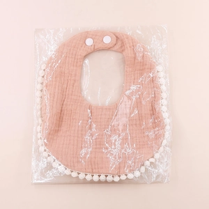Detail view of pink cotton muslin baby bib with white pom-pom trim and snap buttons