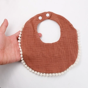 Brown cotton gauze baby bib with white pom-pom trim and adjustable snap buttons