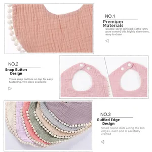 Detail of cotton gauze baby bib featuring pom-pom trim and adjustable snap fasteners