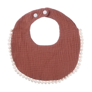 Detail of rust red cotton gauze baby bib with white pom-pom trim and snap buttons