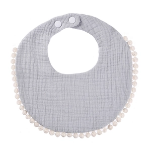 Detail of grey muslin cotton baby bib featuring soft pom-pom trim and adjustable snap buttons