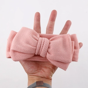 Détail d'un bandeau rose côtelé pour bébé avec un grand nœud sur fond blanc éclatant