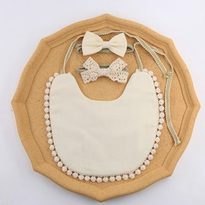 Detailed set of soft baby bib with pom-pom lace and matching headbands on cork board