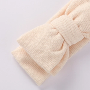 Détail de la texture gaufre douce et du nœud papillon sur ce bandeau bébé crème
