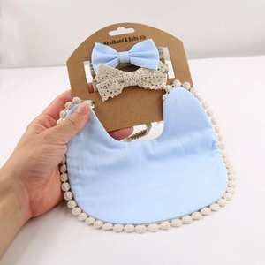 Close-up of baby blue boho bib with cream pom-poms and two matching bow headbands
