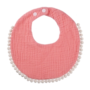 Detail of pink cotton baby bib with decorative white pompom fringe and snaps