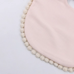 Detail of pink cotton baby bib featuring soft fabric and cream pom-pom lace edge