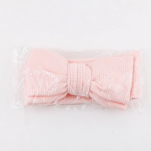 Gros plan d'un bandeau rose pour bébé avec nœud texturé sous sachet plastique