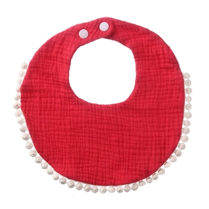 Close-up of soft red cotton gauze baby bib with white pom-pom trim and snap buttons