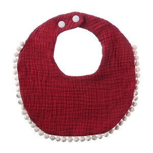 Detail view of burgundy muslin cotton baby bib featuring white pompom trim and snap buttons