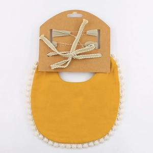 Detail of soft ginger baby bib with white pompom trim and green bow headband on card