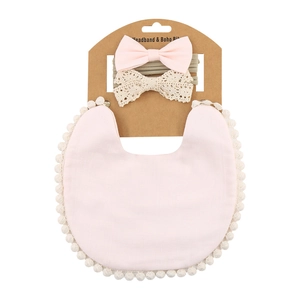 Close-up of baby bib set with plush pom-poms and two bow headbands on kraft card