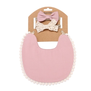 Pink cotton bib with white lace trim and two bow headbands on a paper display card