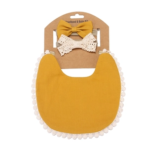 Detail of baby ginger cotton bib with lace trim and two matching bow headbands on kraft card