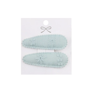 Detailed close-up of light blue fabric hair clips with floral embroidery on white card