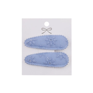 Detail of light blue fabric hair clips with white floral embroidery on display card