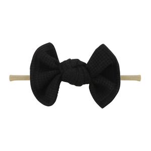 Close-up of black waffle fabric bow and skin-tone elastic nylon headband for babies