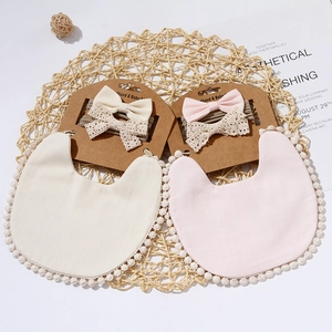 Bamboo cotton baby bib set with lace edges and matching bow headband on woven mat