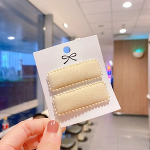 Close-up of rectangular beige knitted hair clips with pearl trim on decorative white card