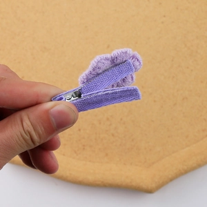 Detail view of purple knitted flower hair clip being held against a cork background
