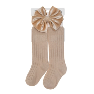 Detailed view of beige ribbed baby sock with a large velvet bow and paper card packaging