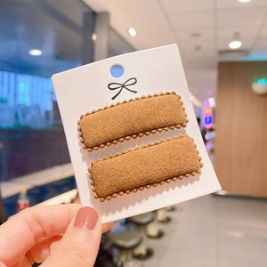 Detailed close-up of brown knit square hair clip with pom-pom trim on display card