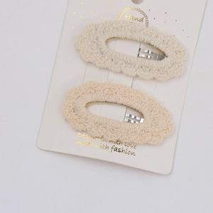 Close-up of two cream knitted lace hair clips with BB clips on white card