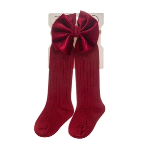 Detail of burgundy ribbed baby socks featuring a large velvet bow on brand packaging