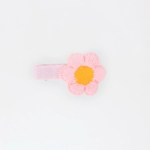 Detailed view of handmade pink knit flower hair clip with yellow center and ribbon cover