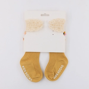 Mustard yellow kids socks with white lace trim on a white packaging board